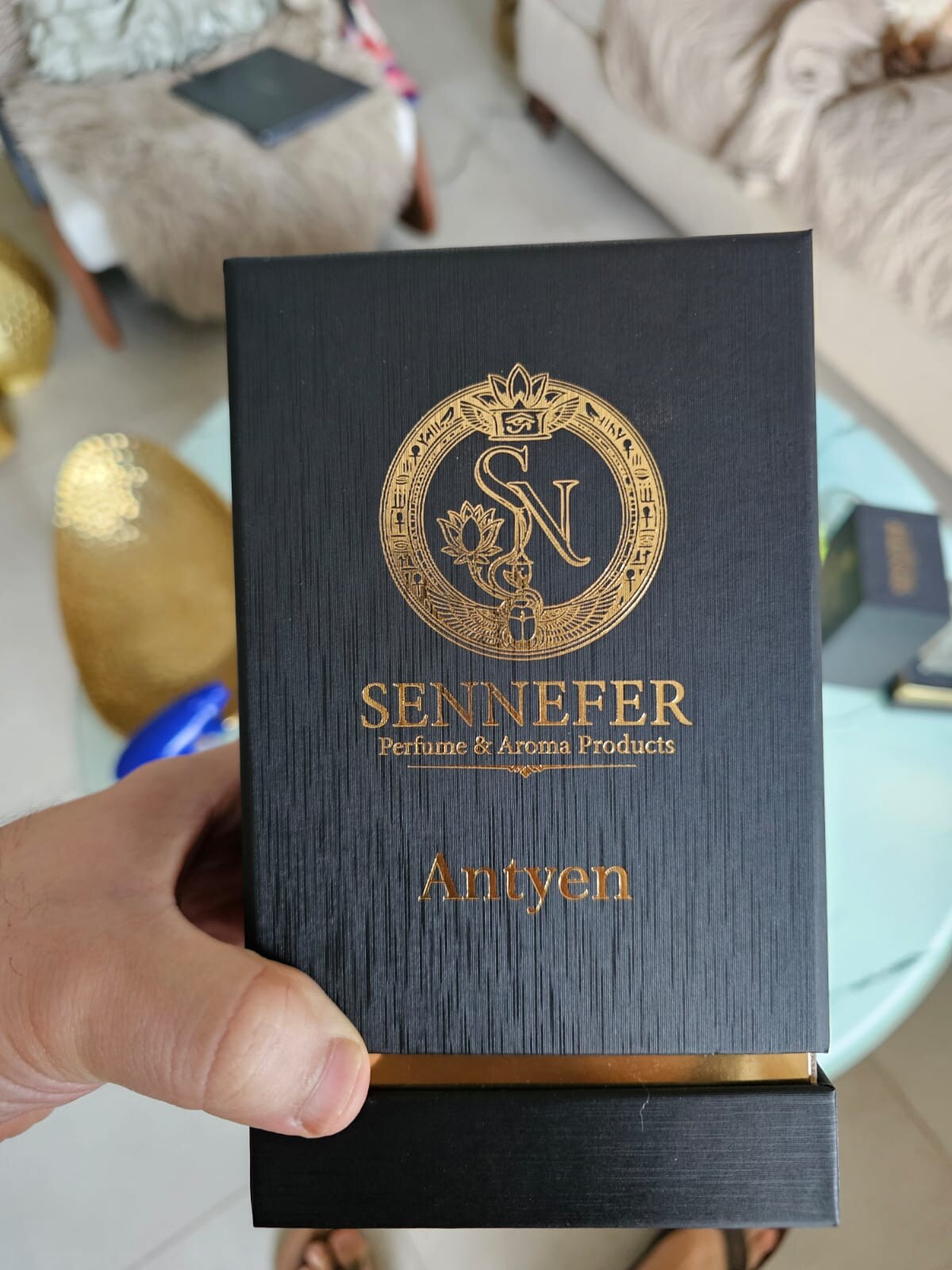 A hand holding the matte black SENNEFER Azeym presentation box